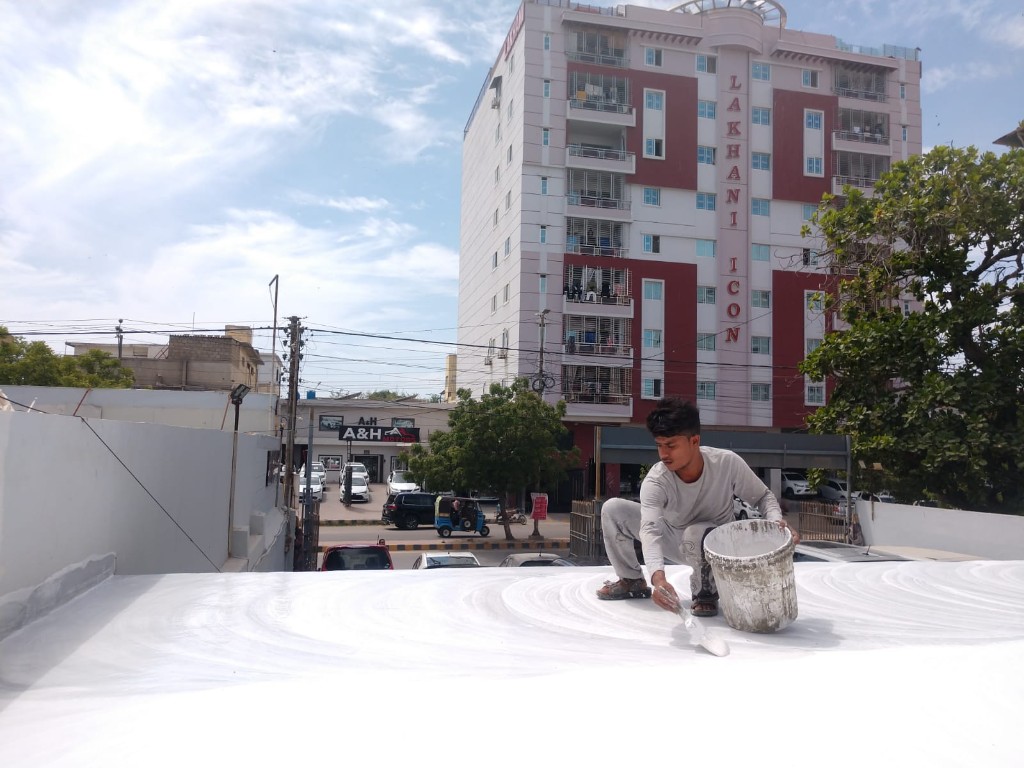 Three workers applying white sealant to a brick-paved residential roof
